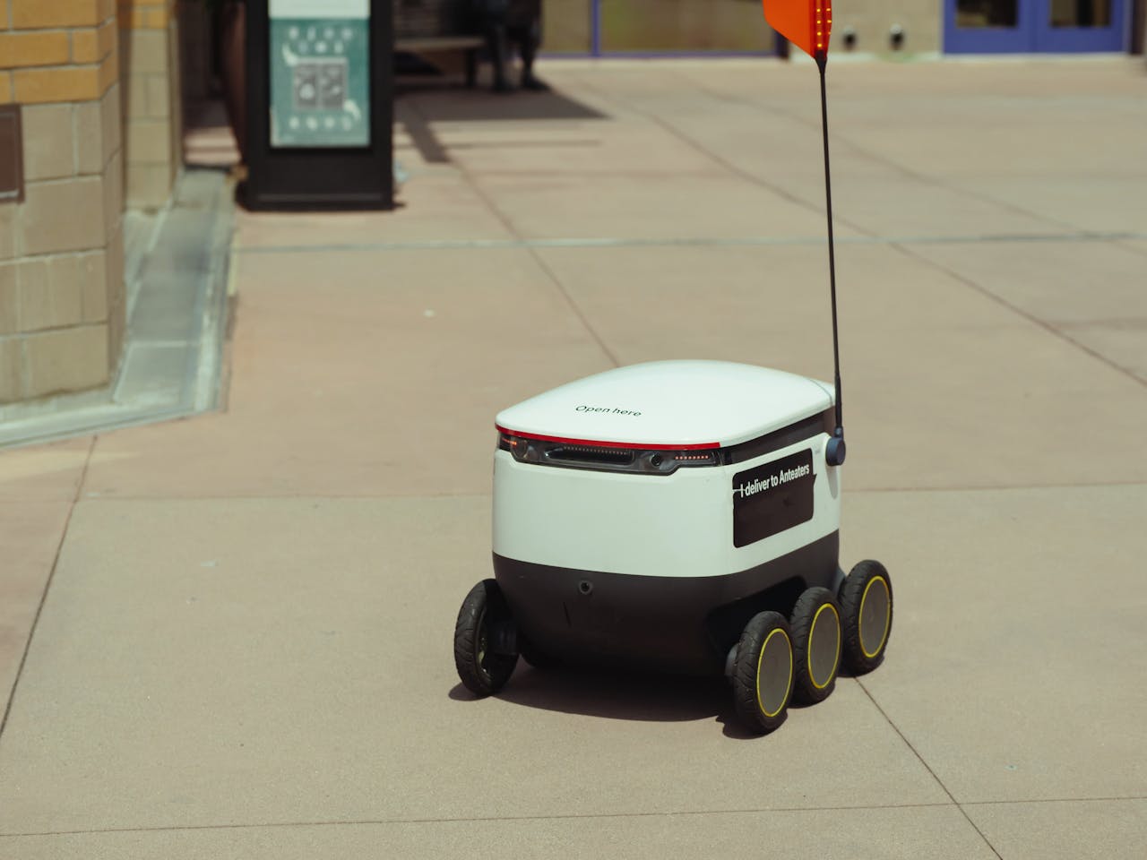 gallery-1 Futuristic autonomous delivery robot navigating a city sidewalk on a sunny day.